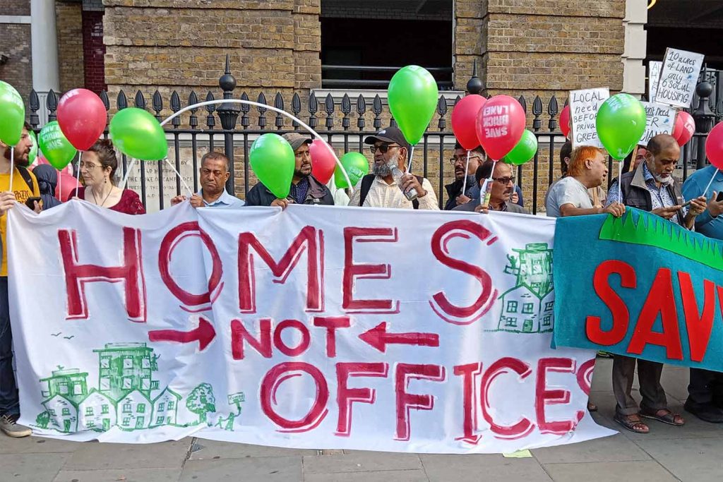 Protesters standing outside with balloons carrying a large sign which reads 'homes not offices'