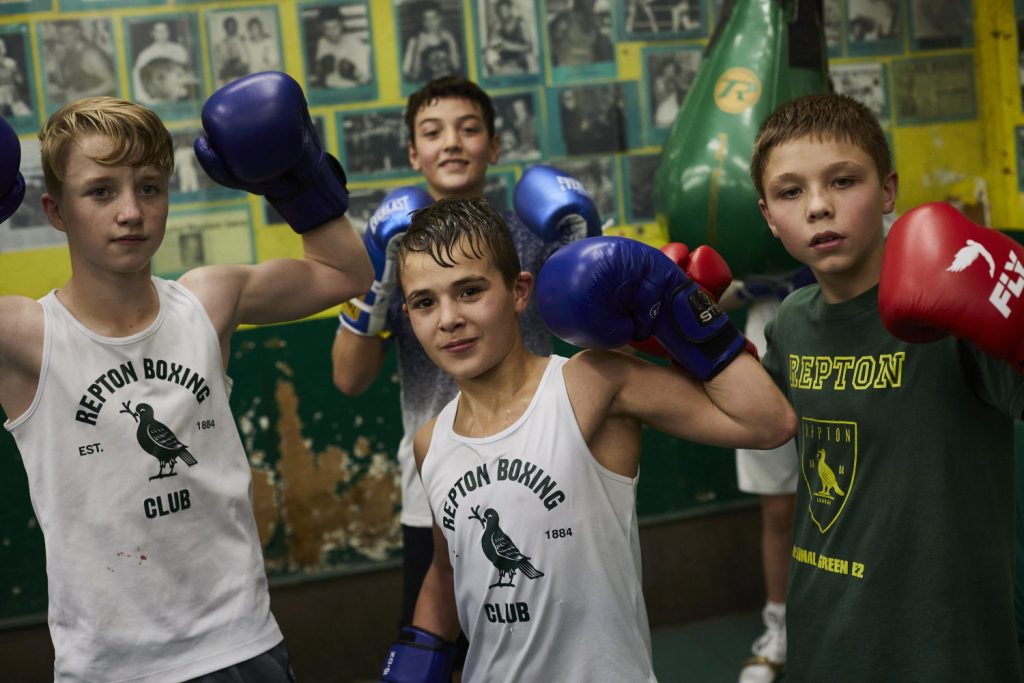 4 younger Repton Boxing Club members hold their fists up in celebration, Bethnal Green.