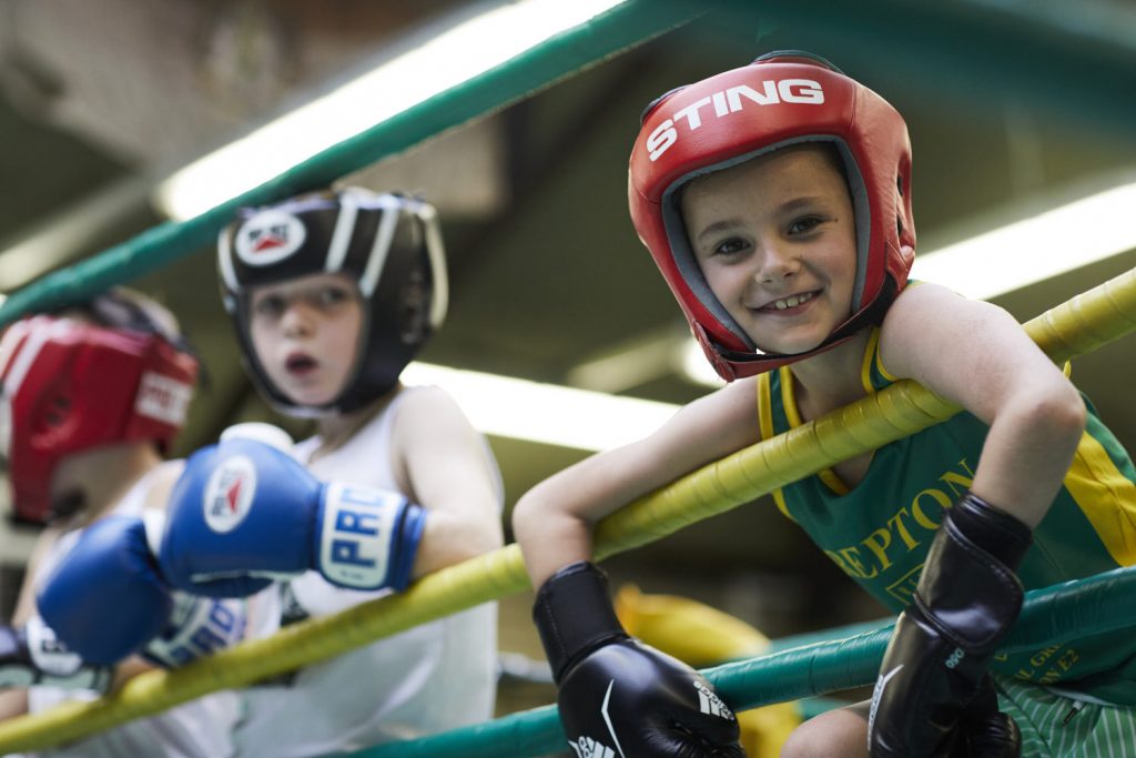 Young Repton Boxing Club boy smiles at the camera from the boxing ring whilst training at the Victorian Bath House