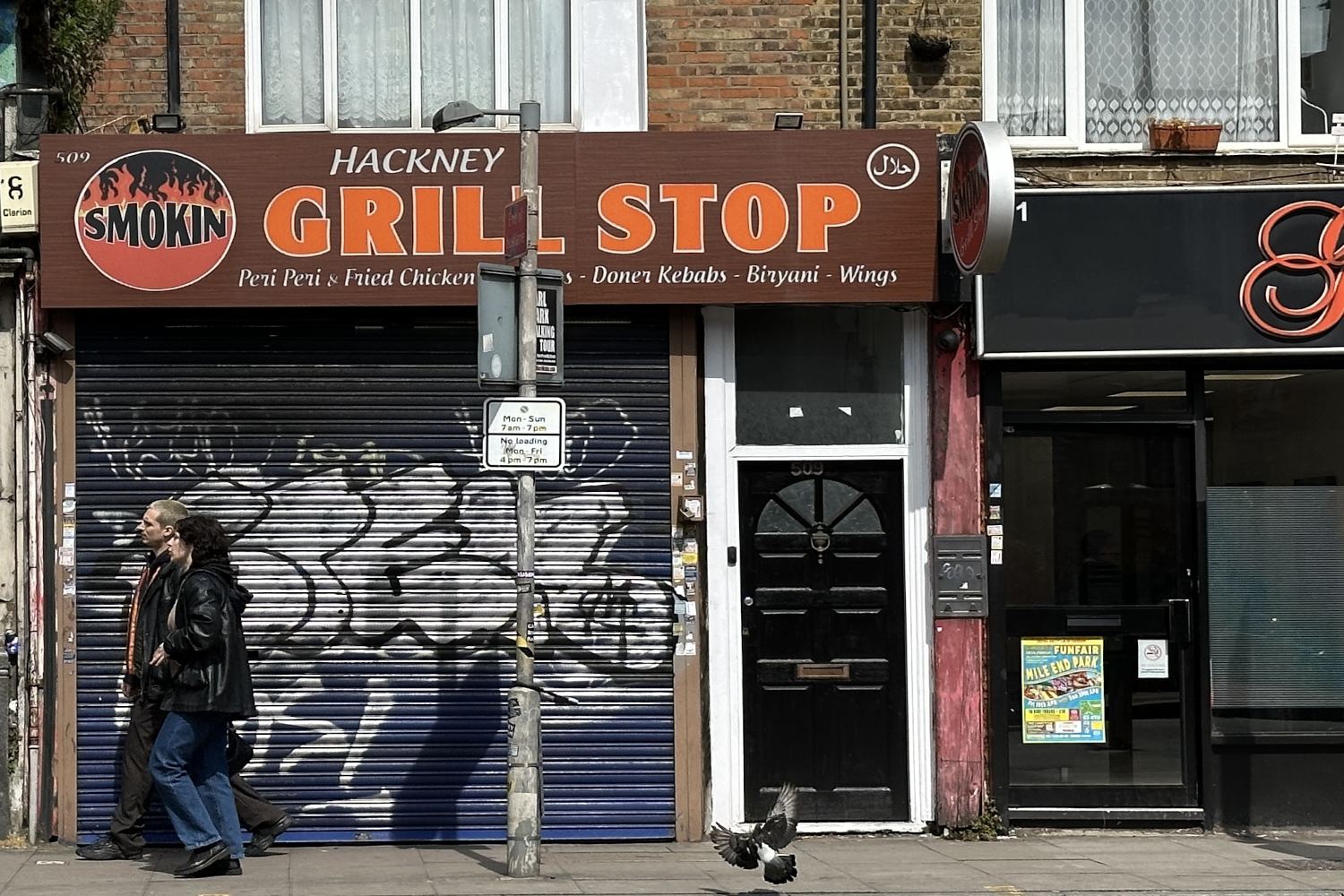Opposite the bus stop, the Hackney Grill Stop sign shows it serves Fried Chicken and Wings.